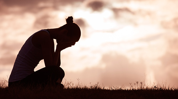 mujer silueta negra sentada en el campo triste con depresión tapándose la cara y llorando en un día oscuro y nublado