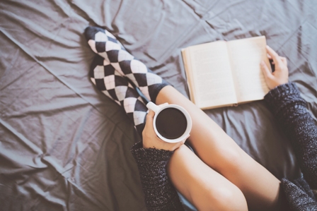 pies de mujer en la cama con cafe y libro leyendo y bebiendo con calcetines de cuadros
