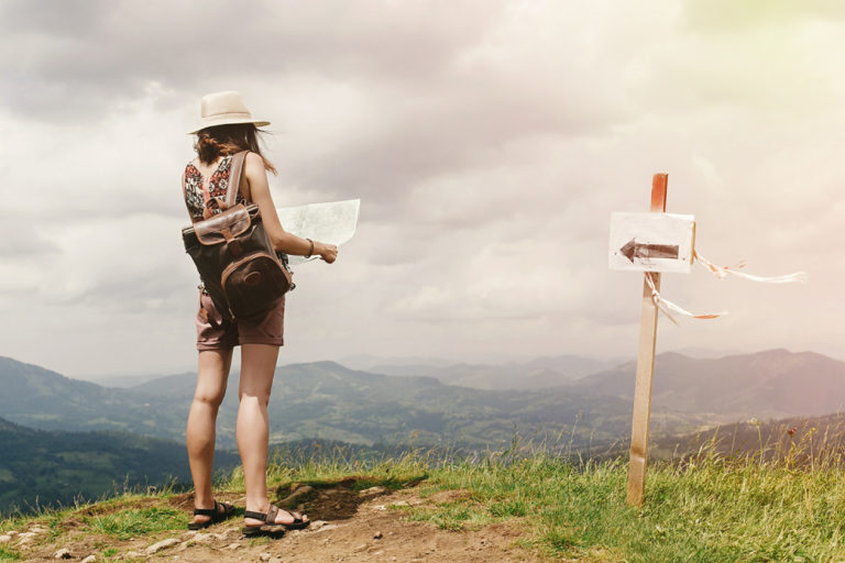 mujer dada la vuelta de espaldas en el campo encima de la montaña mirando un mapa para no perderse y guiarse