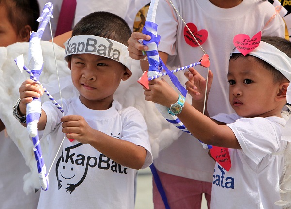 dos niños asiáticos con camisetas blancas de kapbata jugando con dos arcos de papel