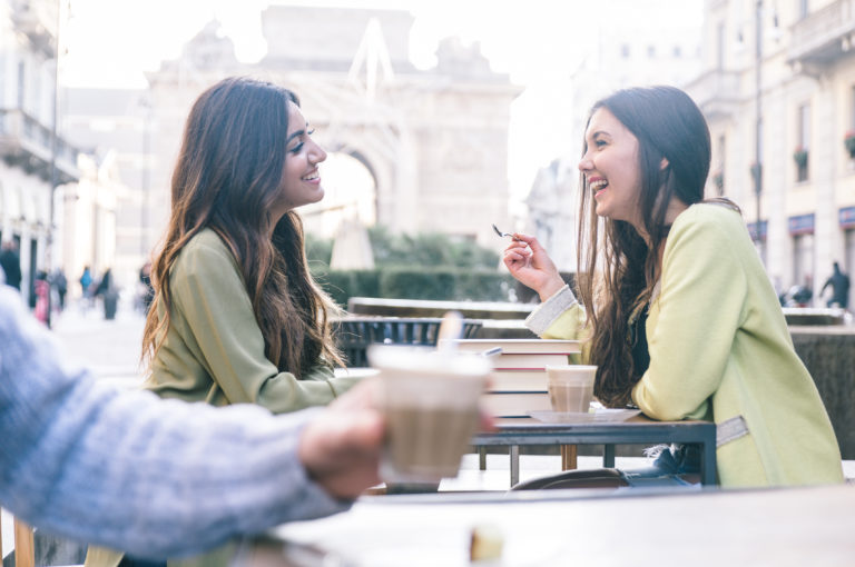 dos chicas vestidas de verde hablando riéndose y felices en un bar terraza tomando un café