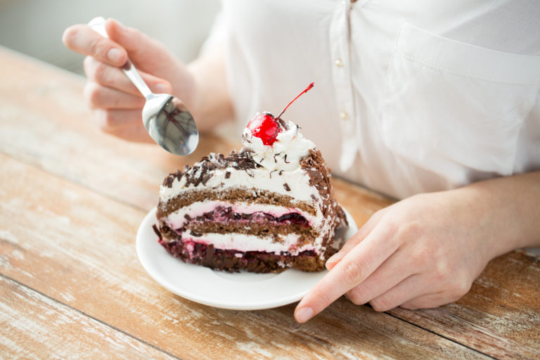 persona mujer vestida de blanco comiendo una tarta de chocolate con cereza guinda del pastel con cuchara sobre una mesa de madera