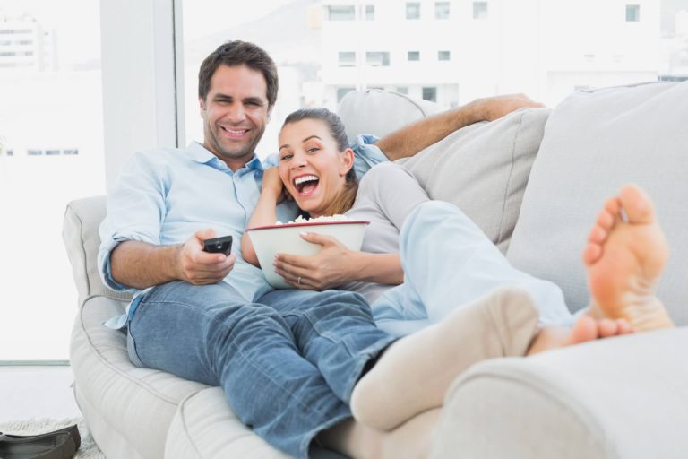 pareja feliz en el sofá viendo una película en la televisión. Comiendo palomitas