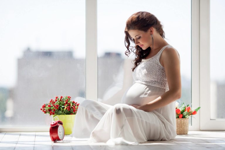 mujer con vestido blanco embarazada con flores rojas y despertador